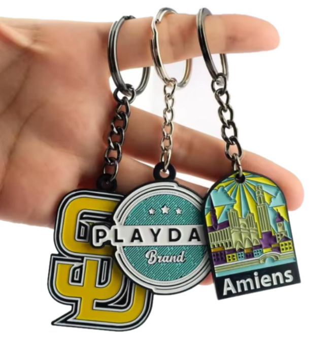 Three custom enamel keychains held in a hand