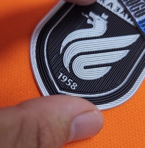 Black and silver TPU crest patch on orange fabric